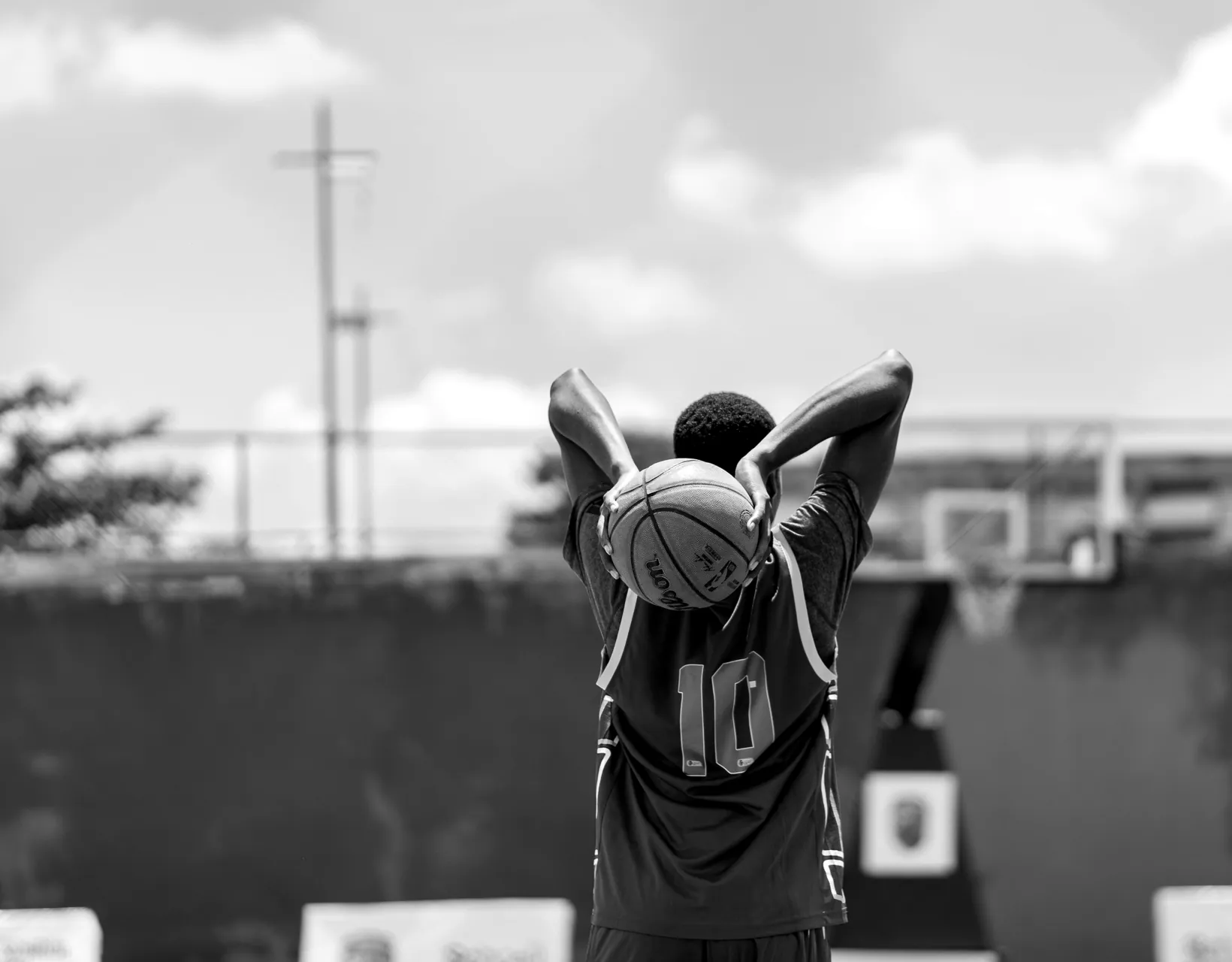 A young player in a number 10 jersey lines up a shot at an outdoor basketball hoop