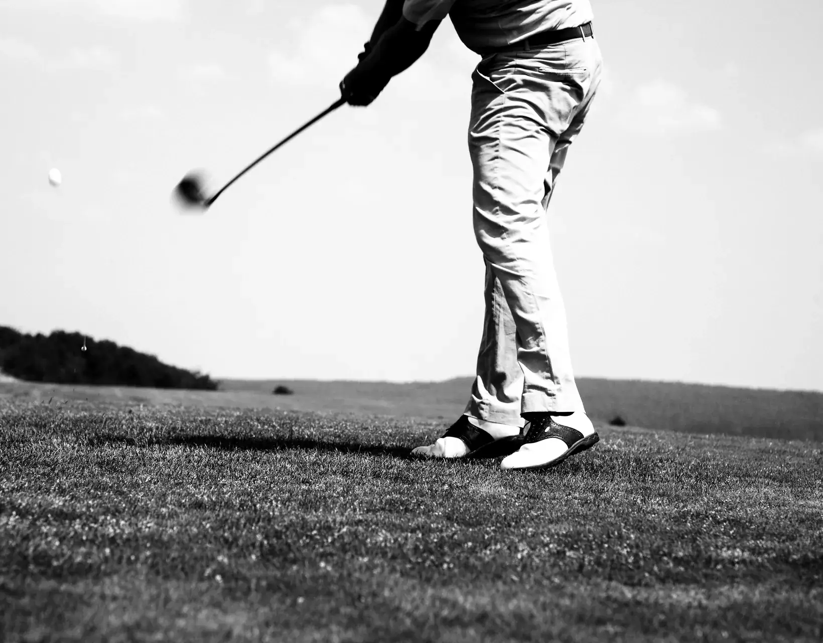 A golfer follows through on a drive, the ball in flight over the fairway