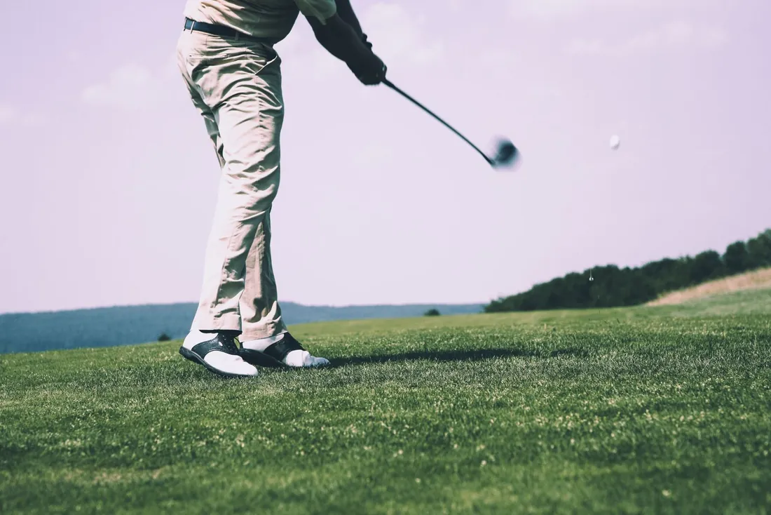 A golfer follows through on a drive, the ball in flight over the fairway