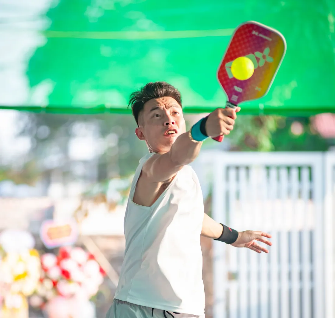 A pickleball player at the net swings a paddle at the ball