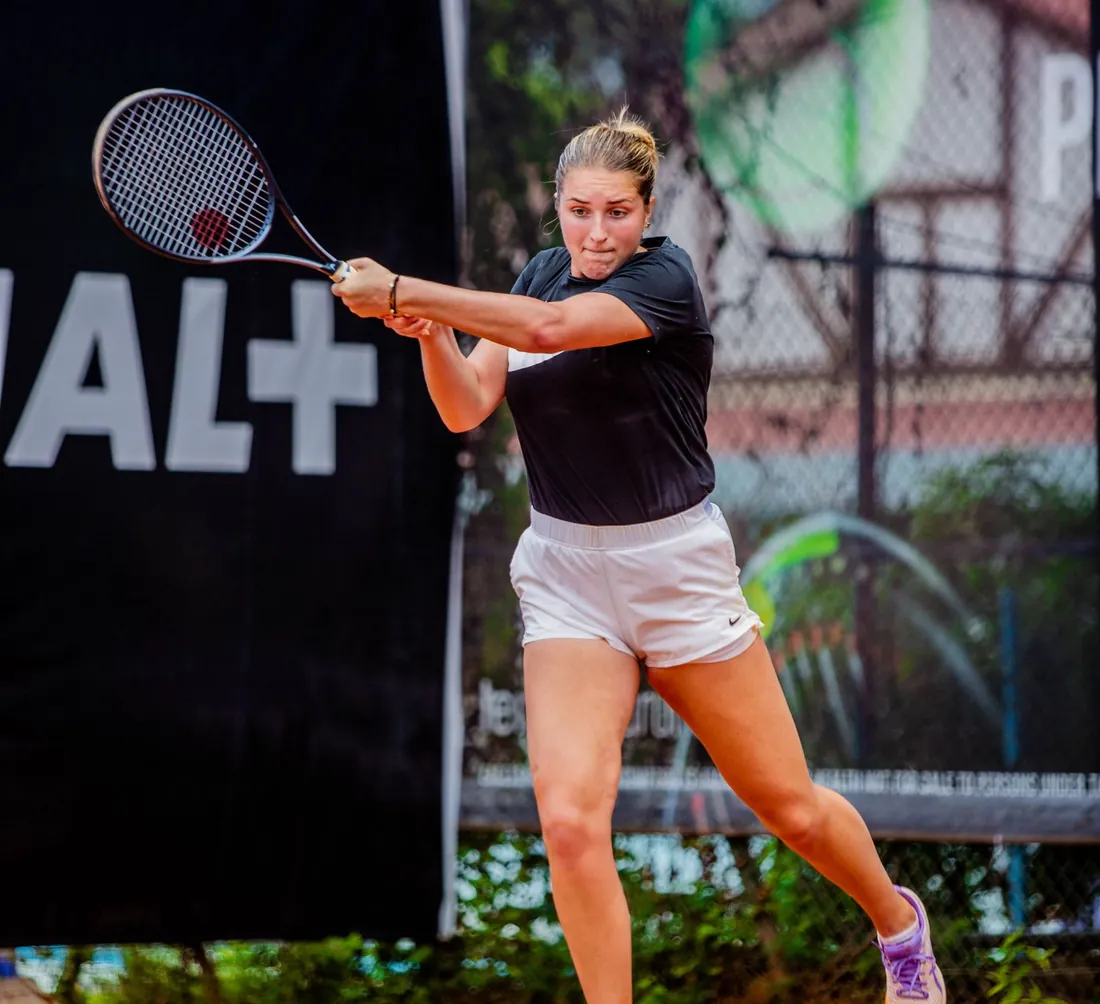 A woman drives a two-handed backhand on a clay tennis court